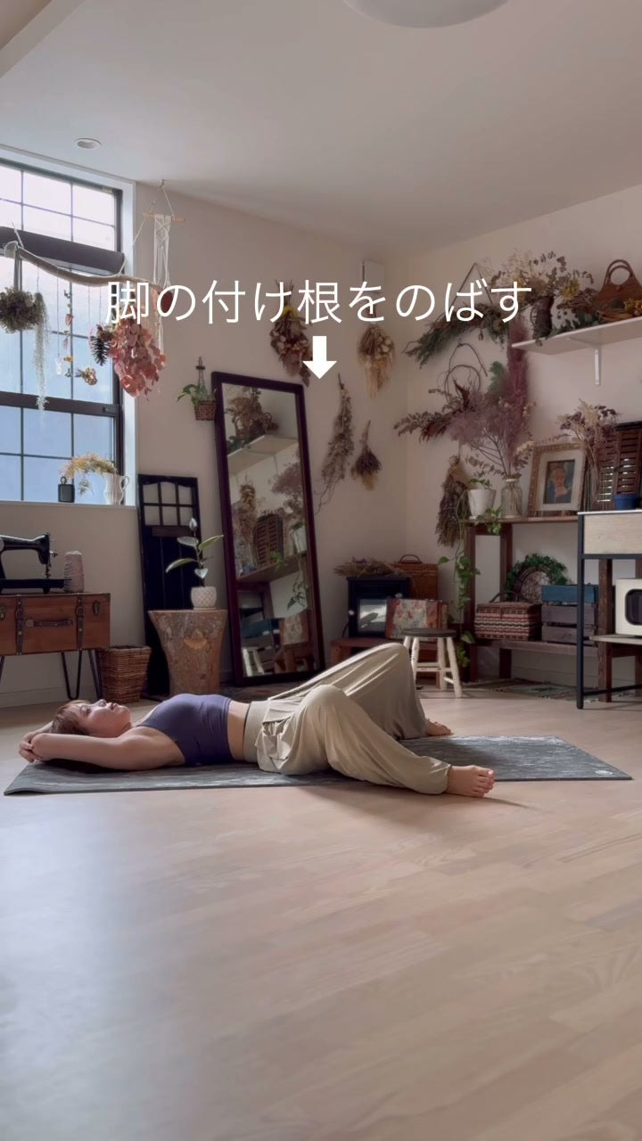 仰向けに寝て両腕を頭上に伸ばし、脚の付け根から全身を長く伸ばすポーズ